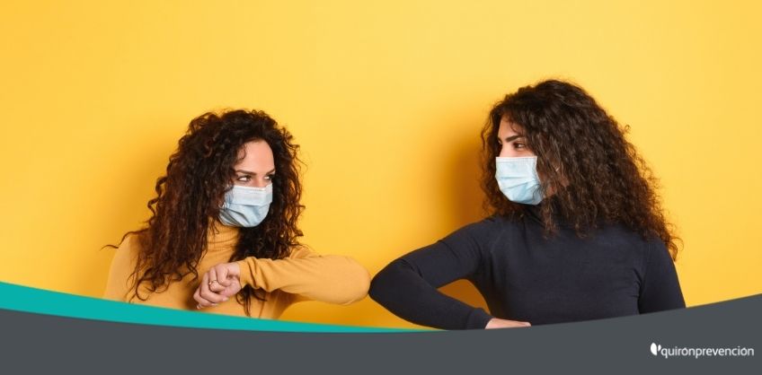 dos mujeres con mascarilla saludándose con el codo imagen grande